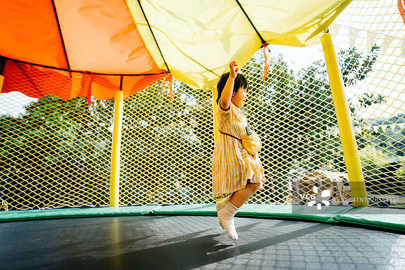 快乐的亚洲小女孩在户外游乐场的充气城堡里开心地笑着跳跃图片素材