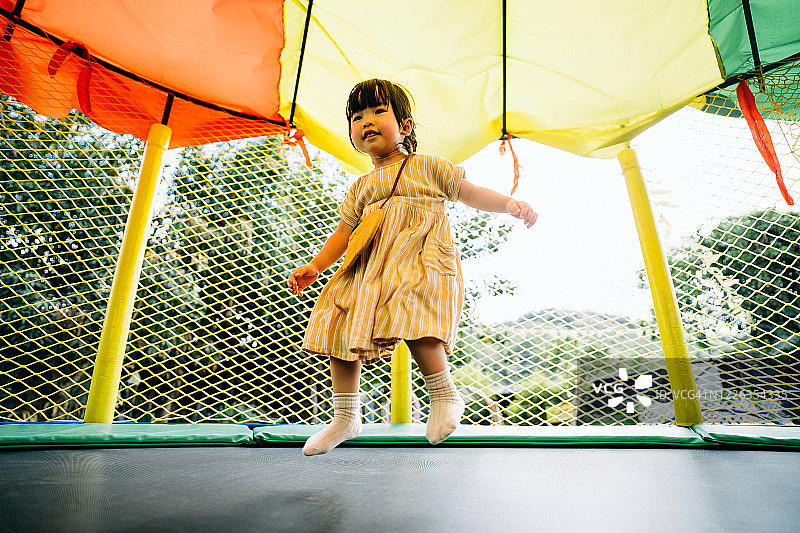 快乐的亚洲小女孩在户外游乐场的充气城堡里开心地笑着跳跃图片素材