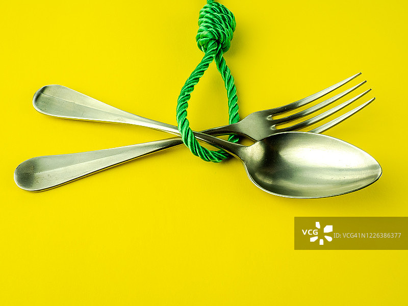 绞刑吏的结、勺子和叉子在黄色背景上，饮食失调概念图片素材