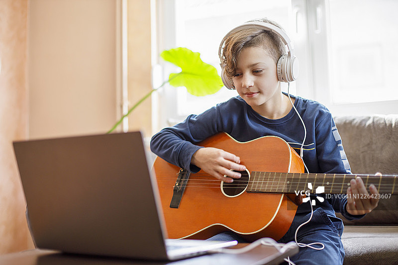 戴着耳机用笔记本电脑学吉他的儿童图片素材