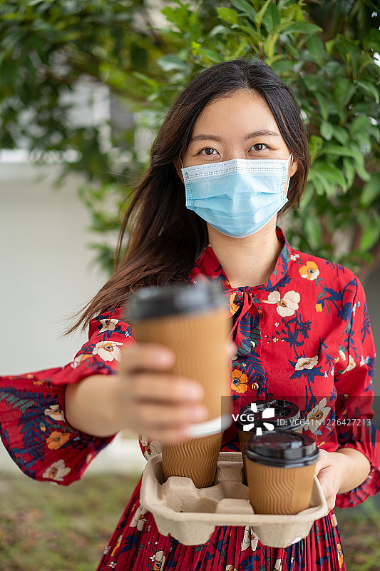 戴口罩手持外卖咖啡杯的年轻女人图片素材