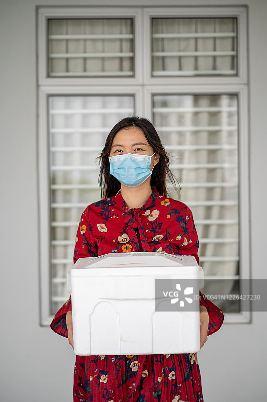 戴口罩手提泡沫储存箱送货的年轻女人图片素材