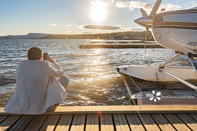 商人坐在水上飞机旁，拿着智能手机图片素材