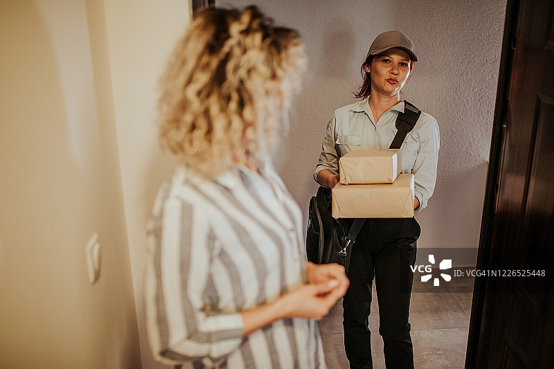 快乐的年轻女人从邮政工作人员那里收到包裹图片素材