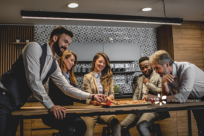 商务人士在办公室厨房附近休息时吃披萨图片素材