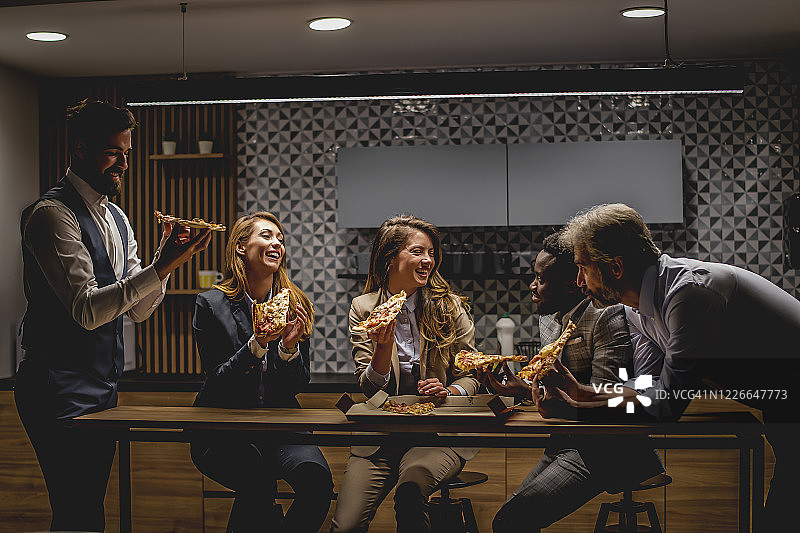 商务人士在办公室厨房附近休息时吃披萨图片素材