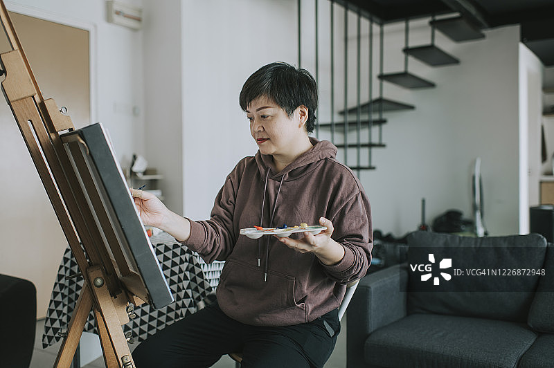 在家用调色板、画笔和画纸在画架上绘画的亚洲女艺术家图片素材