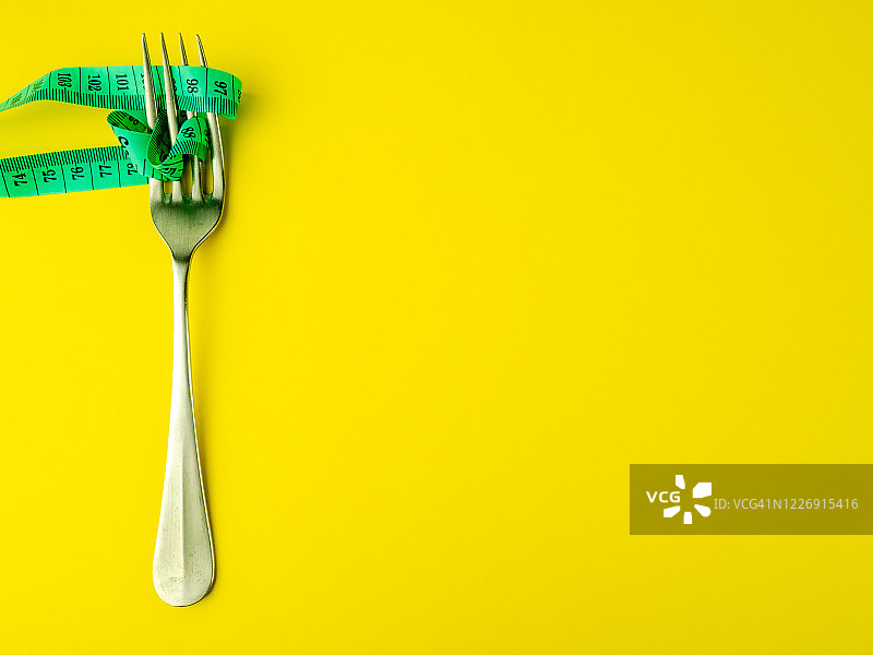 黄色背景上的叉子和卷尺，饮食和肥胖概念图片素材
