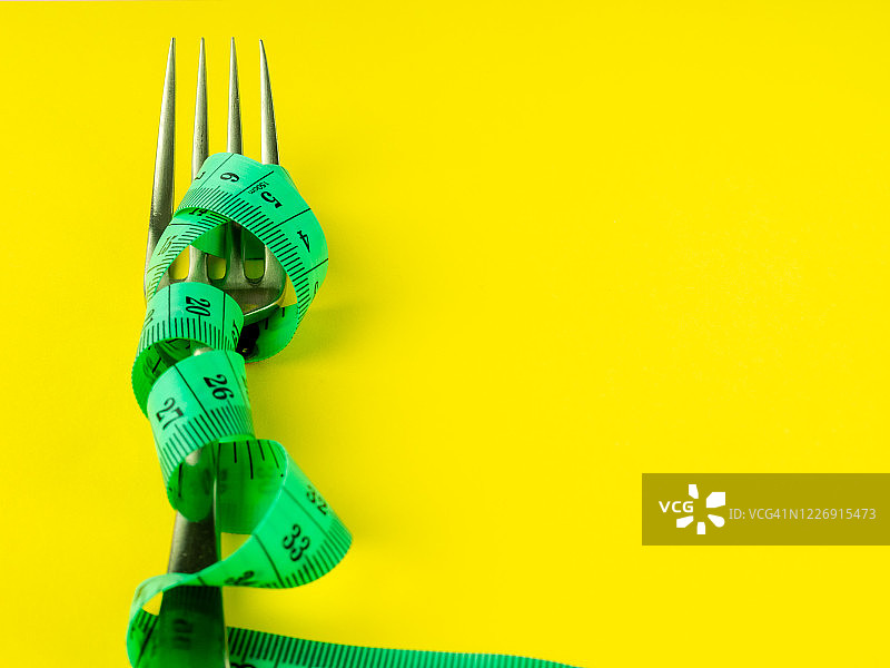 黄色背景上的叉子和卷尺，饮食和肥胖概念图片素材