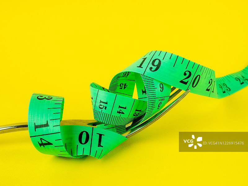 黄色背景上的叉子和卷尺，饮食和肥胖概念图片素材