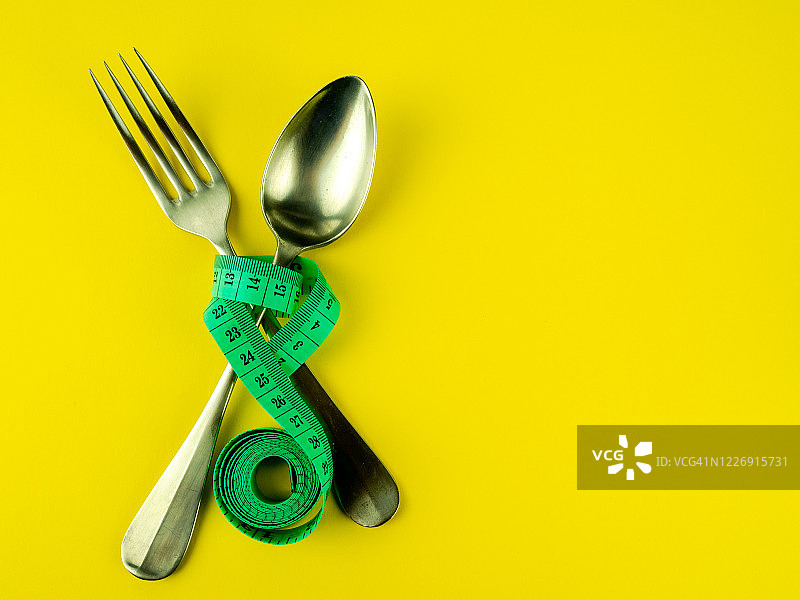 黄色背景上的叉子、勺子和卷尺，饮食与肥胖概念图片素材