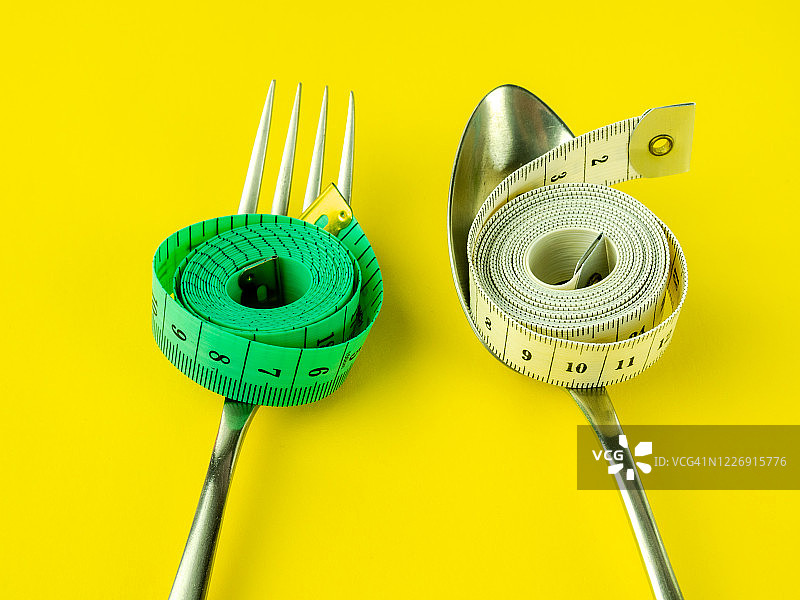 黄色背景上的叉子、勺子和卷尺，饮食与肥胖概念图片素材