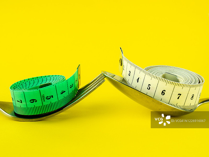 黄色背景上的叉子、勺子和卷尺，饮食与肥胖概念图片素材