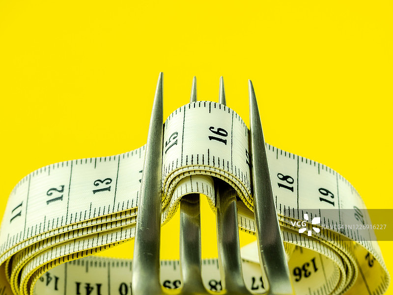 黄色背景上的叉子和卷尺，饮食和肥胖概念图片素材