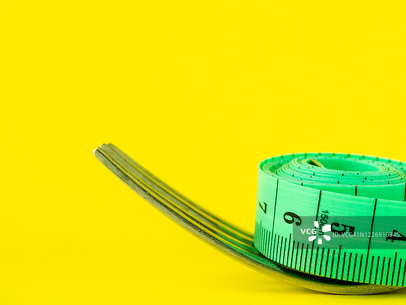 黄色背景上的叉子和卷尺，饮食和肥胖概念图片素材