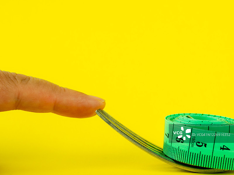 手指触摸叉子和黄色背景上的卷尺，饮食与肥胖概念图片素材