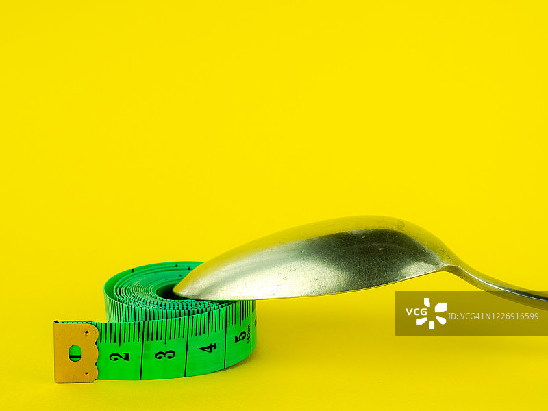 黄色背景上的勺子和卷尺：饮食与肥胖概念图片素材
