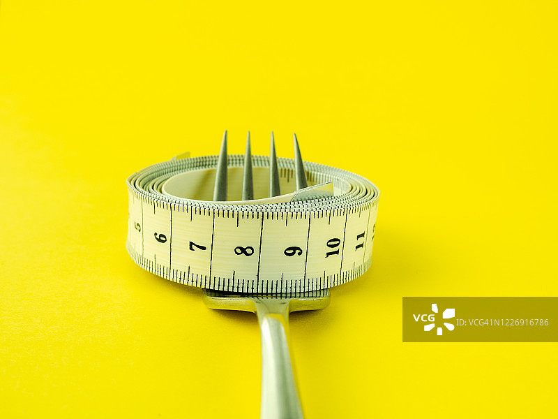 黄色背景上的叉子和卷尺，饮食和肥胖概念图片素材