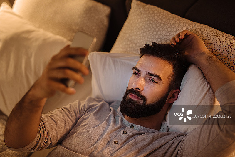 晚上在床上用手机的英俊胡须男图片素材