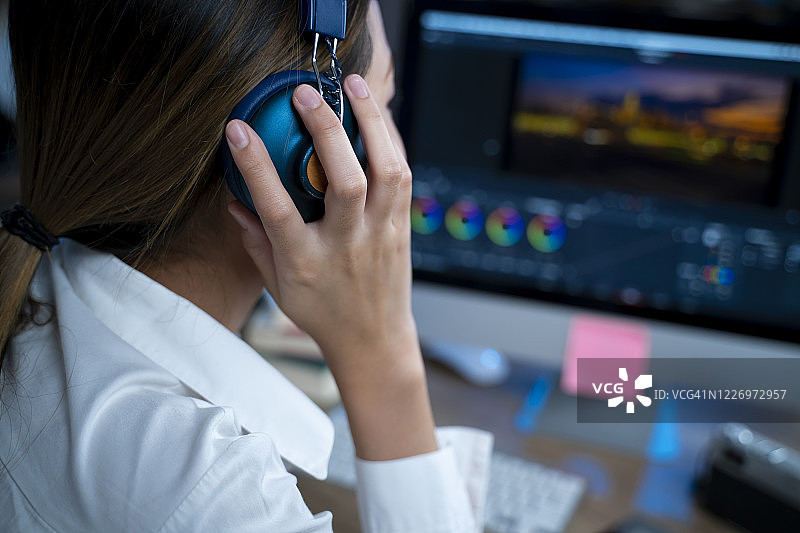 戴着耳机在电脑上进行视频编辑图片素材