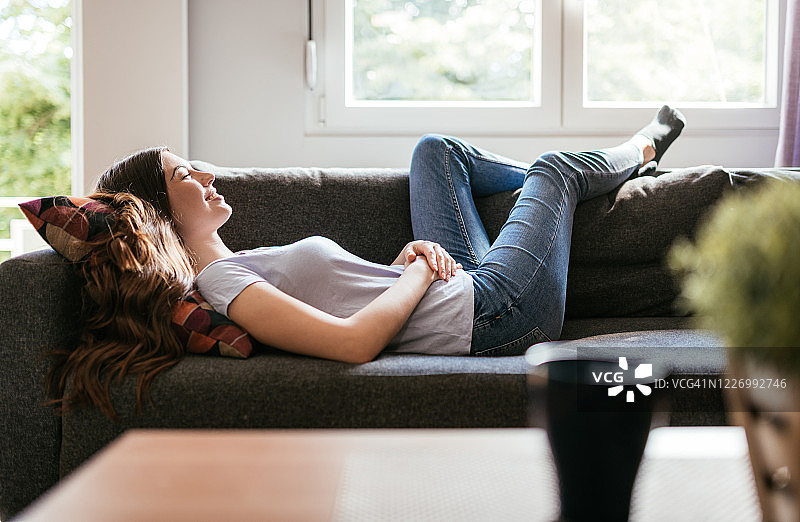 快乐的年轻女人在家中沙发上做白日梦图片素材