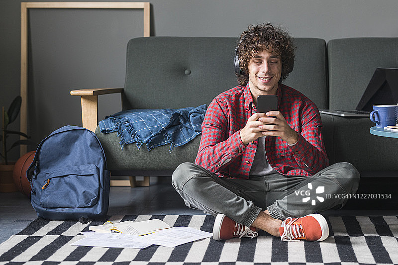 在家里使用手机的快乐年轻人，身穿红色休闲格子衬衫图片素材