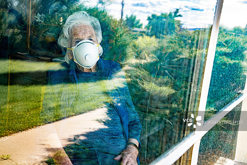 悲伤年长的白人妇女望着窗外感到孤独，在寒冷和流感季节佩戴N95防护口罩以预防新冠病毒SARS nCoV 19冠状病毒猪流感H7N9流感疾病的传播图片素材