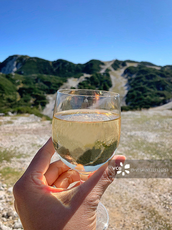 手持白葡萄酒杯，背景是山脉图片素材