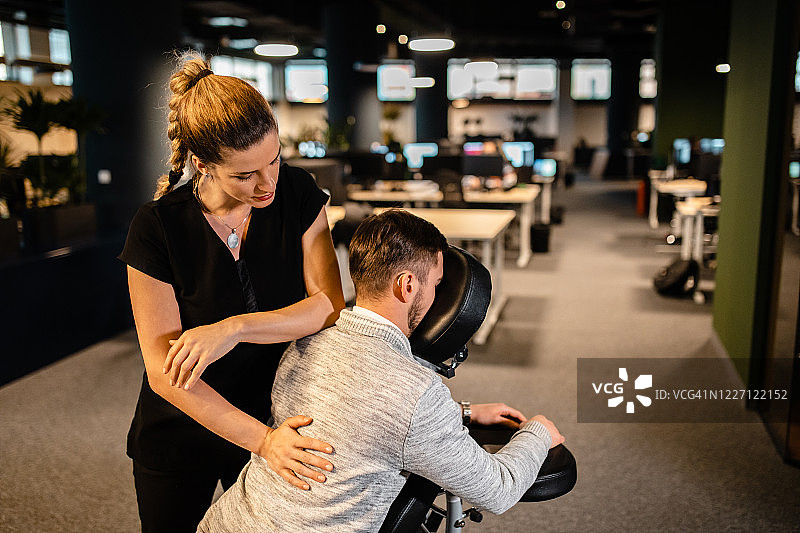 疲惫的网页设计师在公司办公室享受背部按摩图片素材