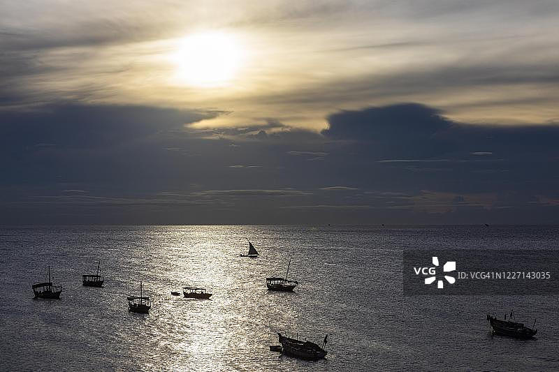 桑给巴尔渔船在雷雨云下的波光粼粼水域中的剪影图片素材