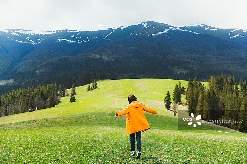 身穿橙色外套的快乐女人跑过美丽的山间草地图片素材