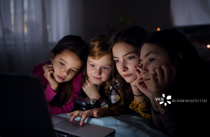 一群小女孩晚上在床上用笔记本电脑看电影图片素材