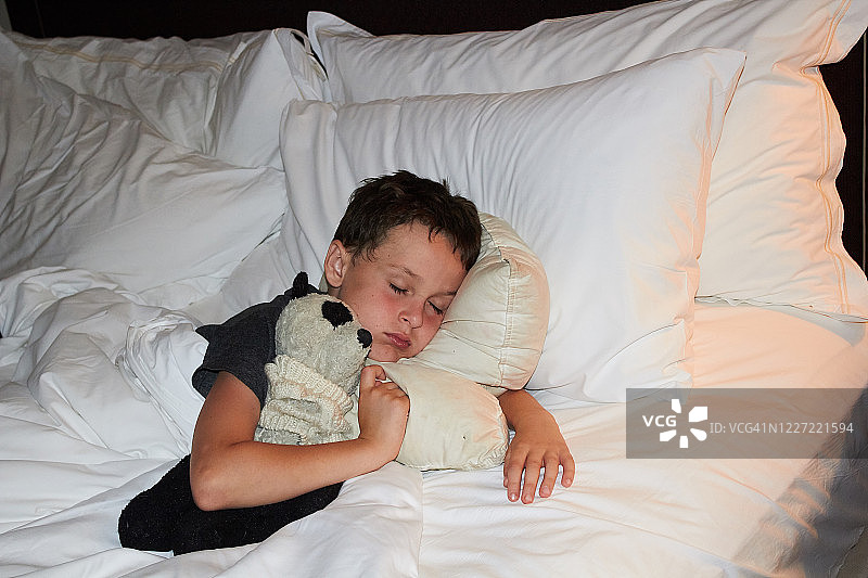 抱着熊猫玩具在床上睡觉的小男孩图片素材