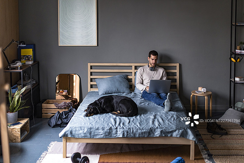 在家学习/工作：在卧室舒适地使用笔记本电脑的年轻人图片素材