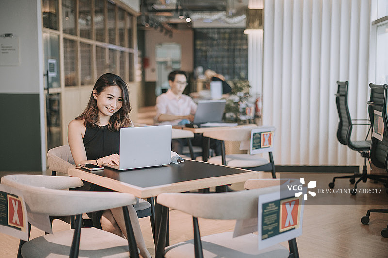 戴着口罩在咖啡馆用笔记本电脑工作并听手机的亚洲自由职业女性图片素材