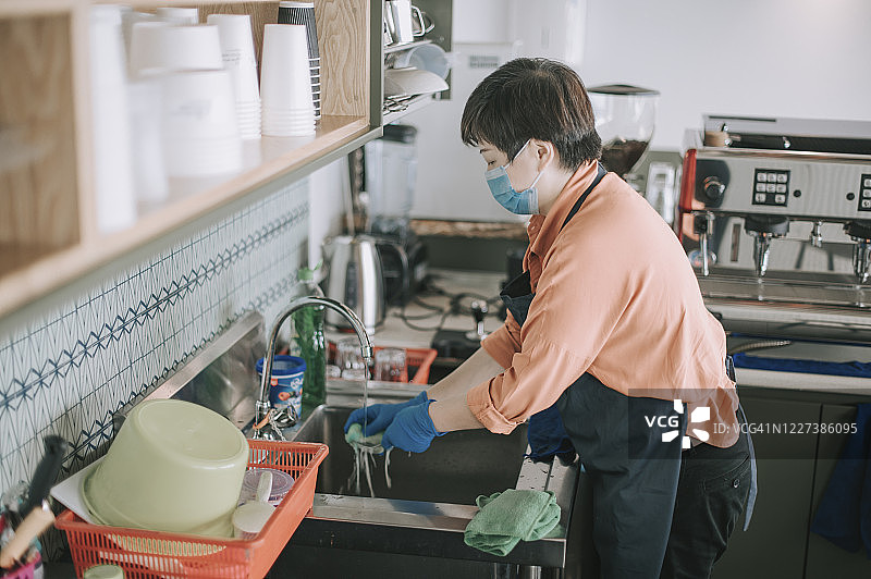 新常态：戴着口罩和手套的亚洲华人小企业主在厨房水槽里洗碗图片素材