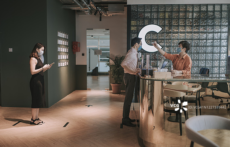 亚洲女接待员测量体温并记录访客个人信息，执行疾病预防标准操作程序图片素材