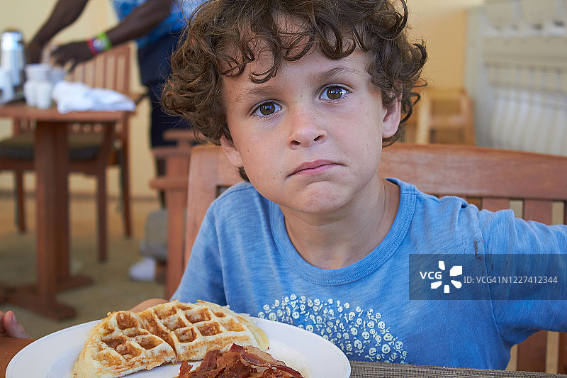 户外咖啡馆里吃华夫饼做鬼脸的小男孩图片素材