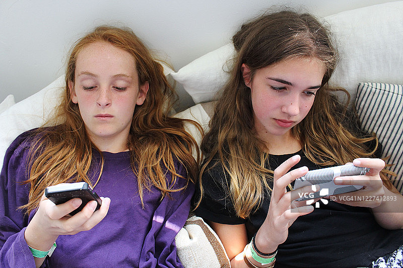 两个少女仰卧在智能手机上玩耍的特写图片素材