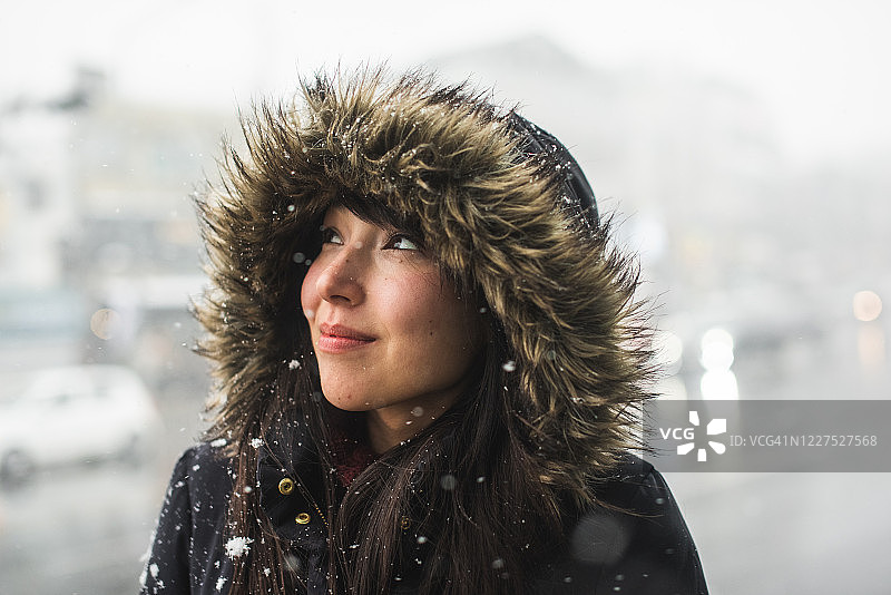 身穿毛皮衬里派克大衣站在雪地里的微笑女性，韩国梨泰院图片素材