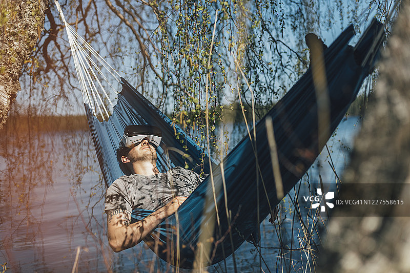 年轻男人在吊床上放松，使用VR眼镜图片素材