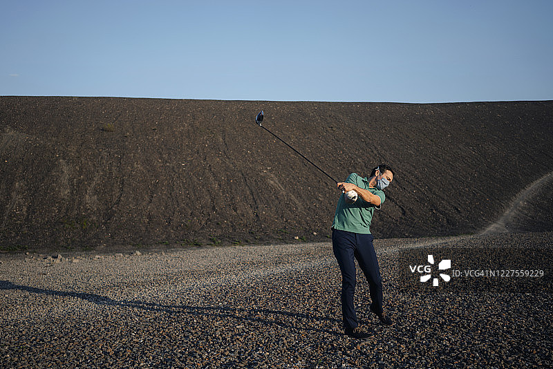 在废弃矿场戴口罩打高尔夫的中年男人图片素材