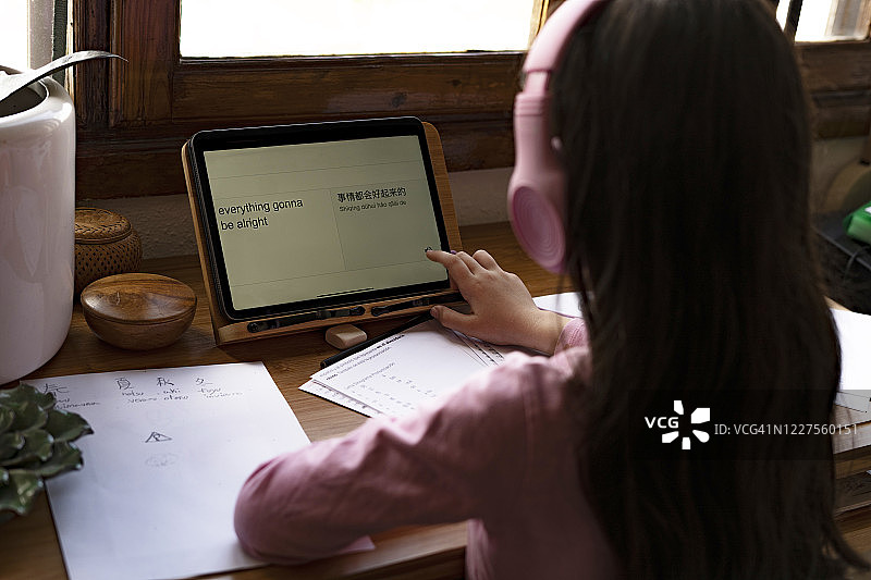 戴着耳机在数字平板电脑上翻译语言，同时在家学习漫画的女孩图片素材