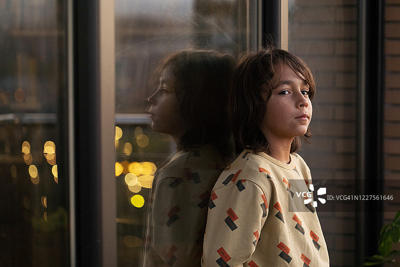 男孩靠在窗户上，玻璃窗映出倒影图片素材