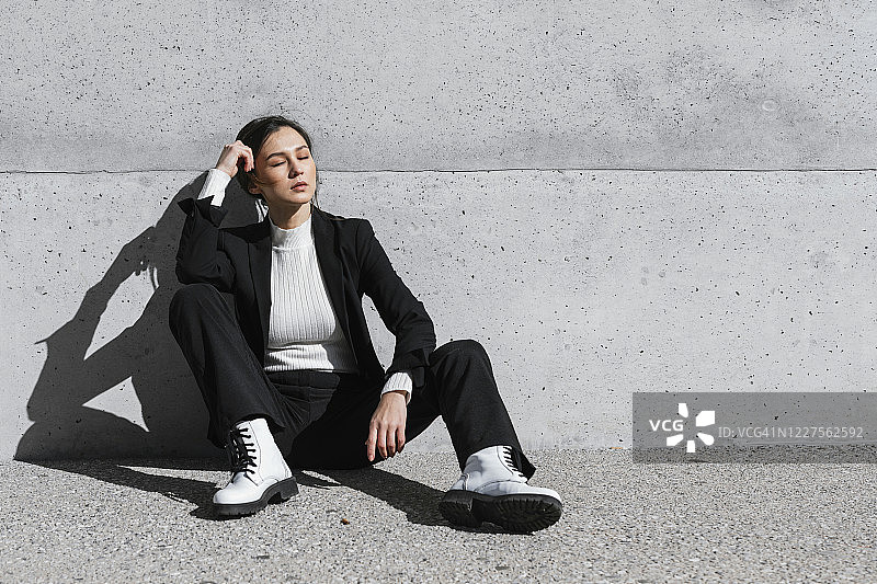 身穿黑色西装坐在水泥墙前的年轻女子图片素材
