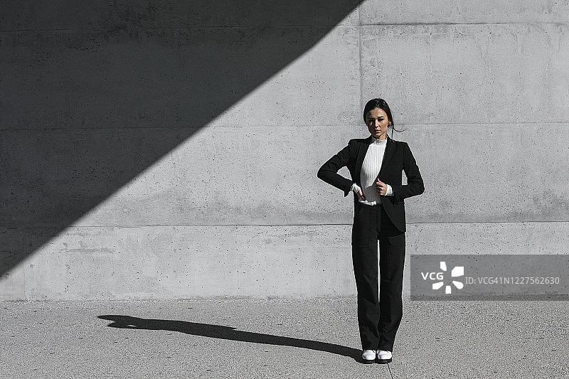 年轻女子穿着黑色西装站在水泥墙前图片素材