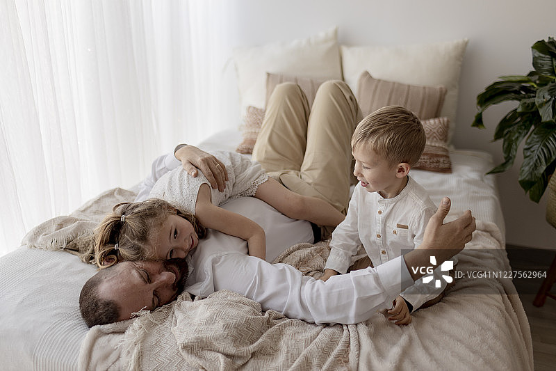 父亲躺在床上与两个孩子依偎图片素材