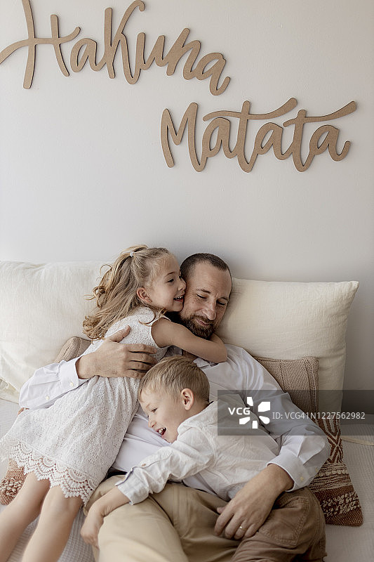 幸福的父亲和两个孩子在家中拥抱的家庭合影图片素材