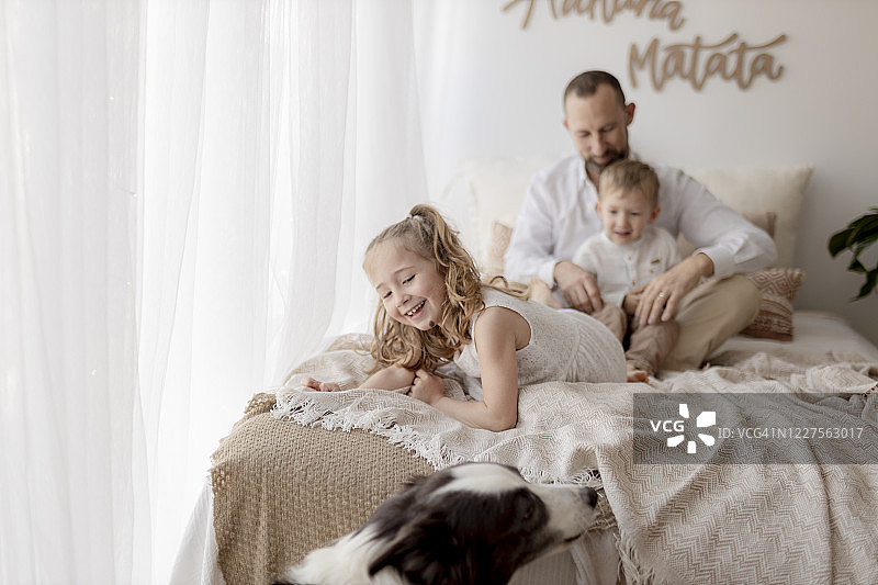 床上微笑小女孩与背景中的父亲和哥哥肖像图片素材