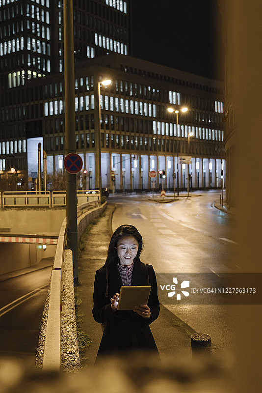 年轻女人在德国法兰克福的城市夜晚使用平板电脑图片素材